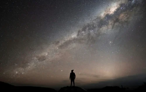 A person standing across the Milky Way galaxy as a backdrop